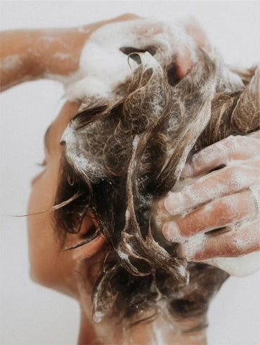 Person washing their hair with soapy hands against a white background