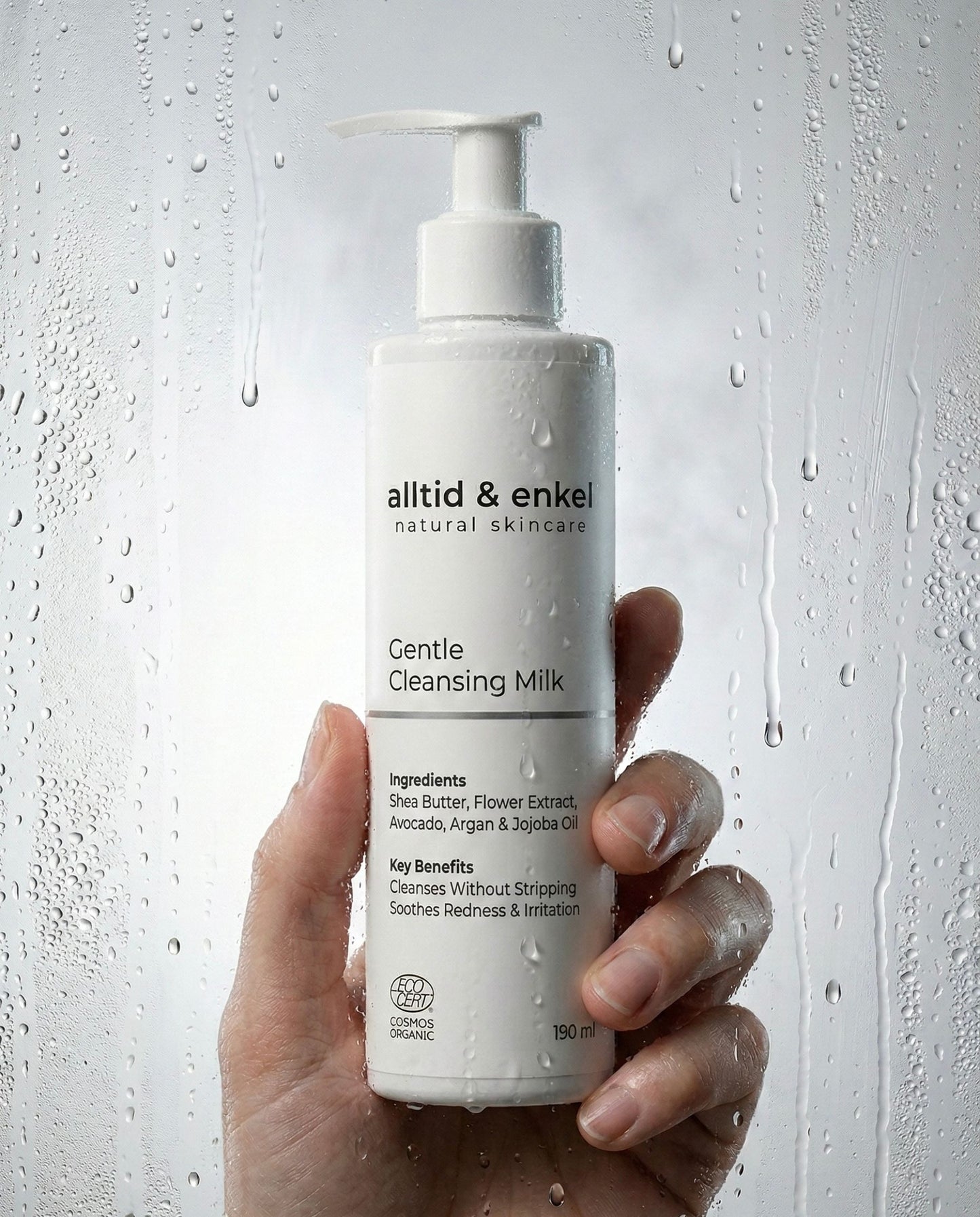 Hand holding a bottle of 'alltid & enkel' Gentle Cleansing Milk against a textured gray background.