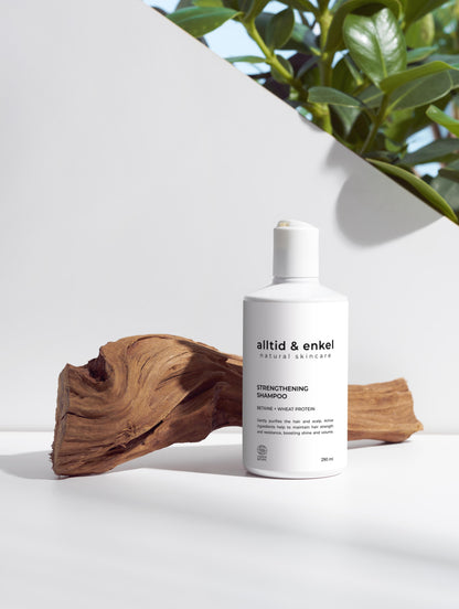 Strengthening shampoo in a sleek white bottle on a white surface with a wooden log, 290 ml.