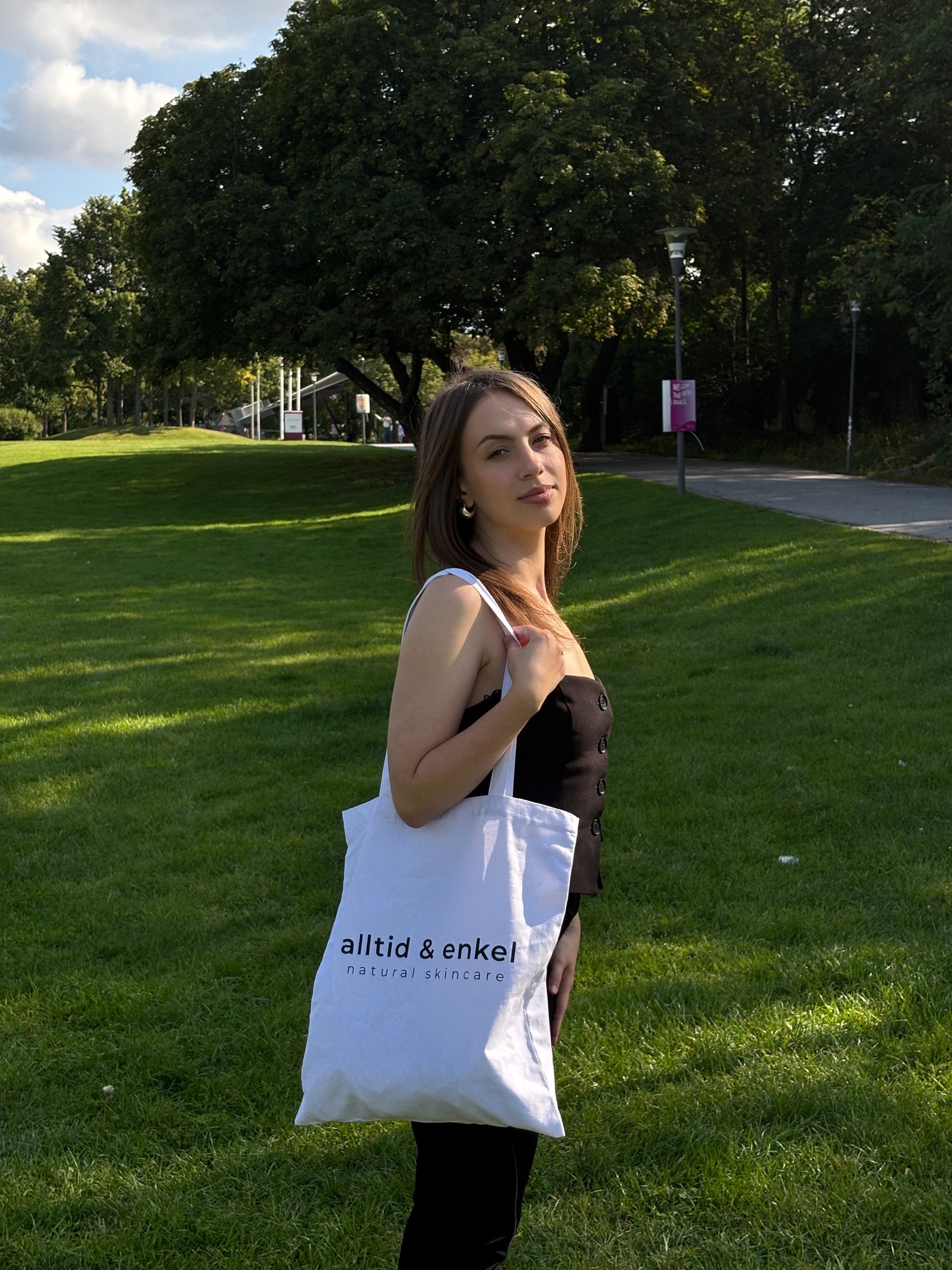 Young woman holding a shopper bag with alltid & enkel logo on it in a grassy area
