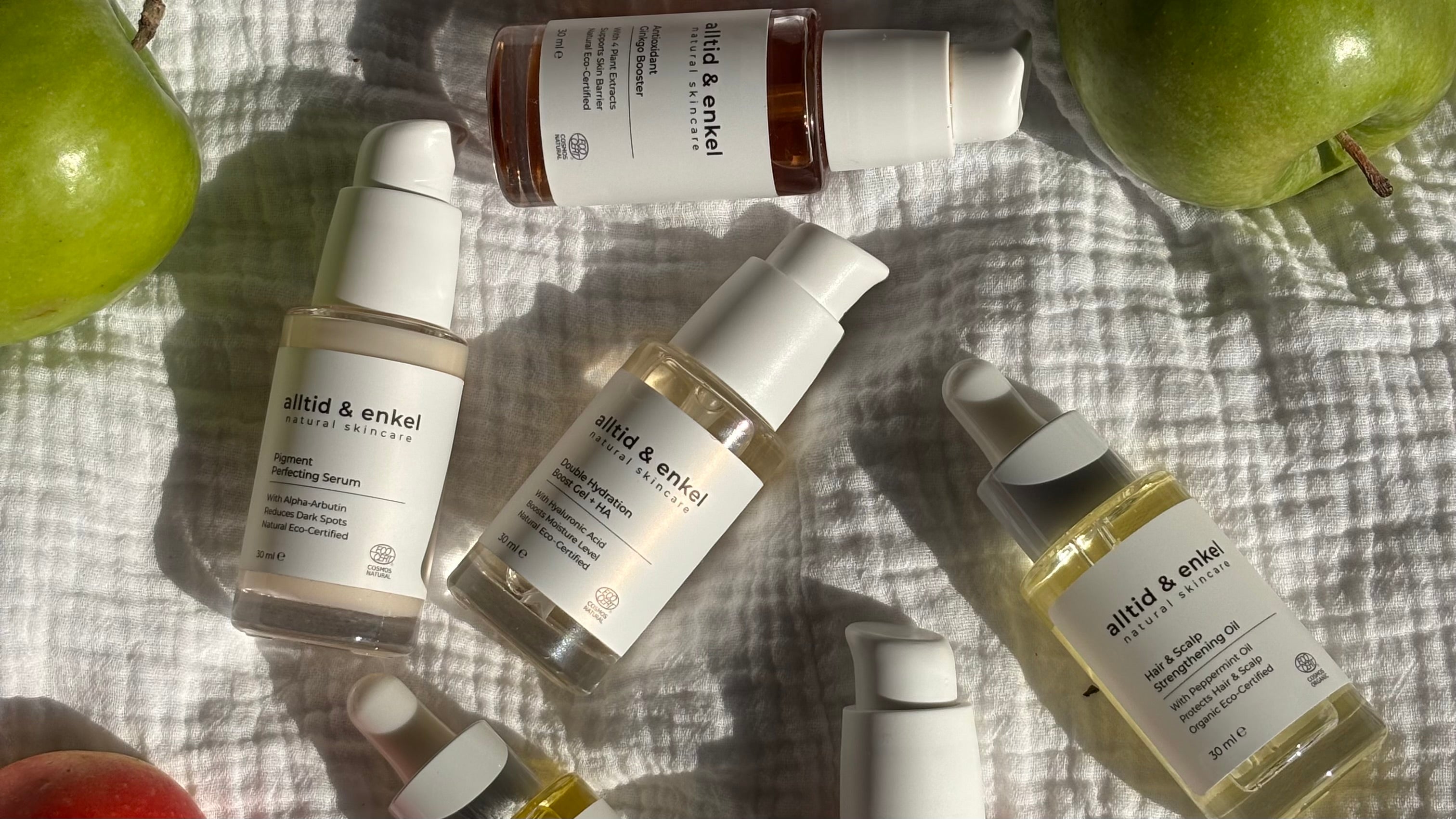 Skincare bottles with visible alltid & enkel brand name on a textured surface with apples