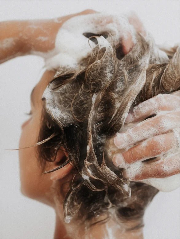 Person washing their hair with soapy hands against a white background