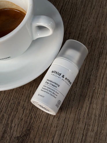 Skincare cream bottle labeled 'alltid & enkel' next to a cup of coffee on a wooden surface