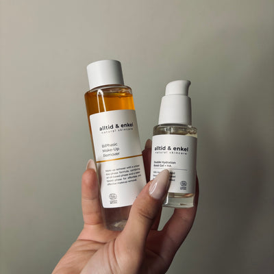 Hand holding two natural skincare bottles against a neutral background