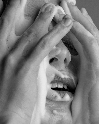 Close-up of a person with hands covering foam on face in black and white.