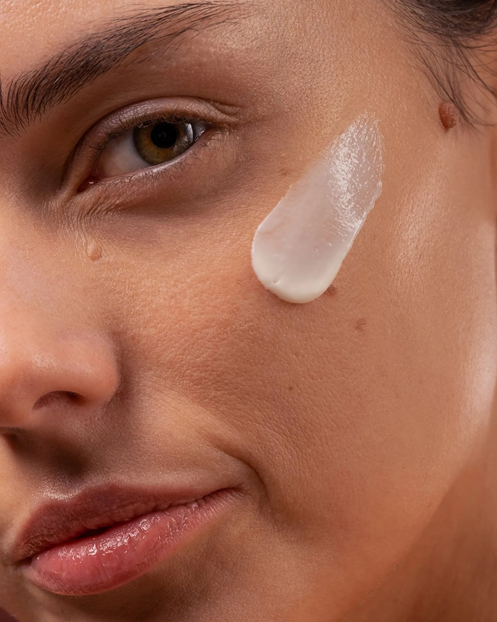 Close-up of a woman's face with a skincare product applied to her cheek.