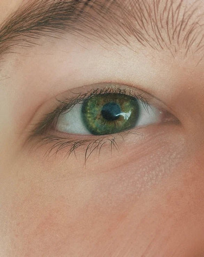 Close-up of a person's green eye with detailed eyelashes and skin texture.