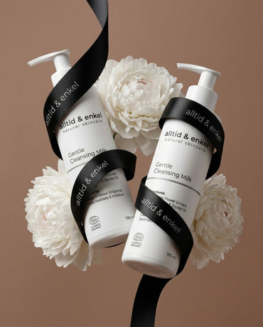 Two bottles of 'alltid & enkel' Gentle Cleansing Milk with white flowers on a brown background