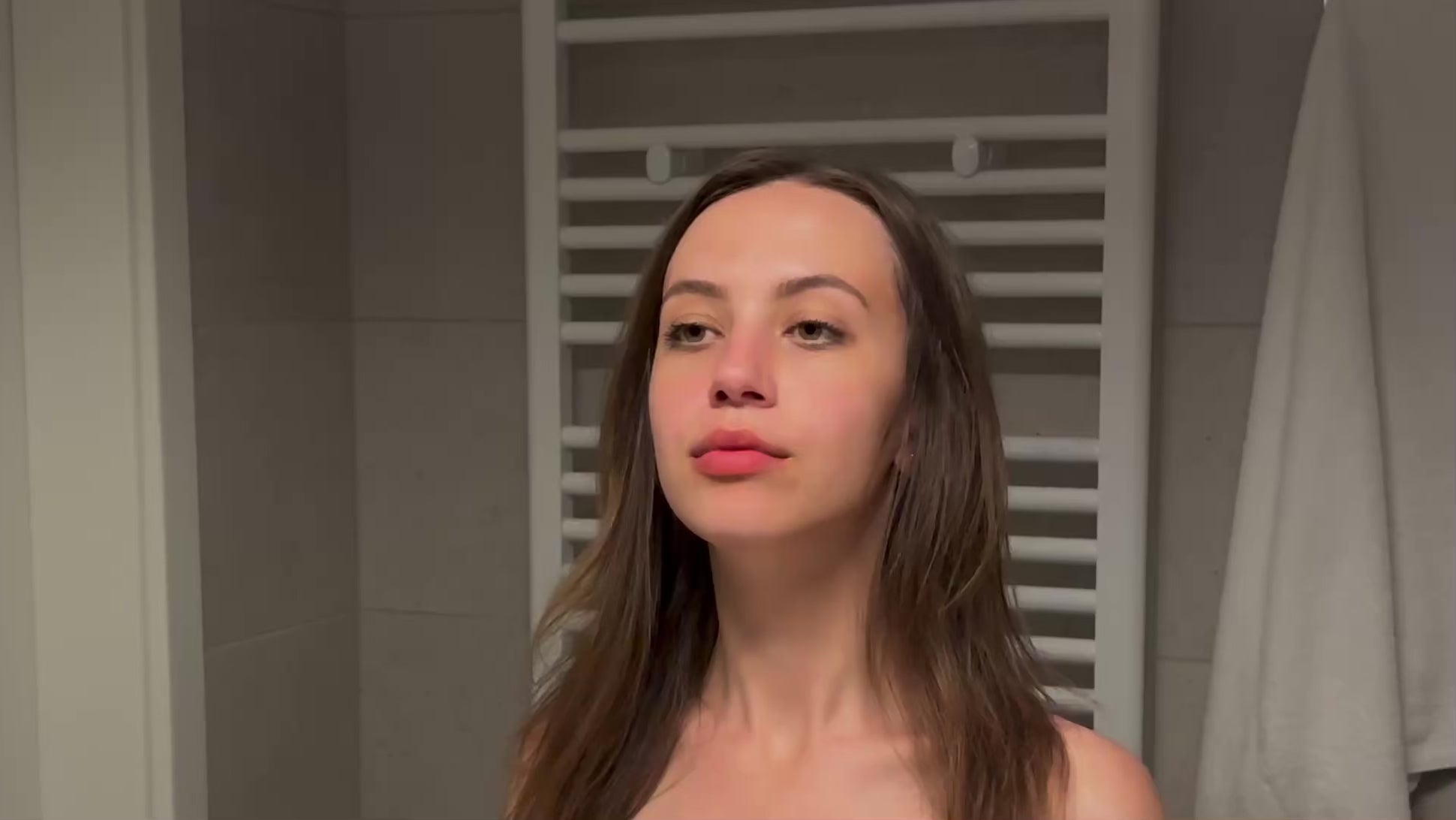 Načíst video: Woman gently applying antioxidant skincare with natural ingredients while standing at a mirror.